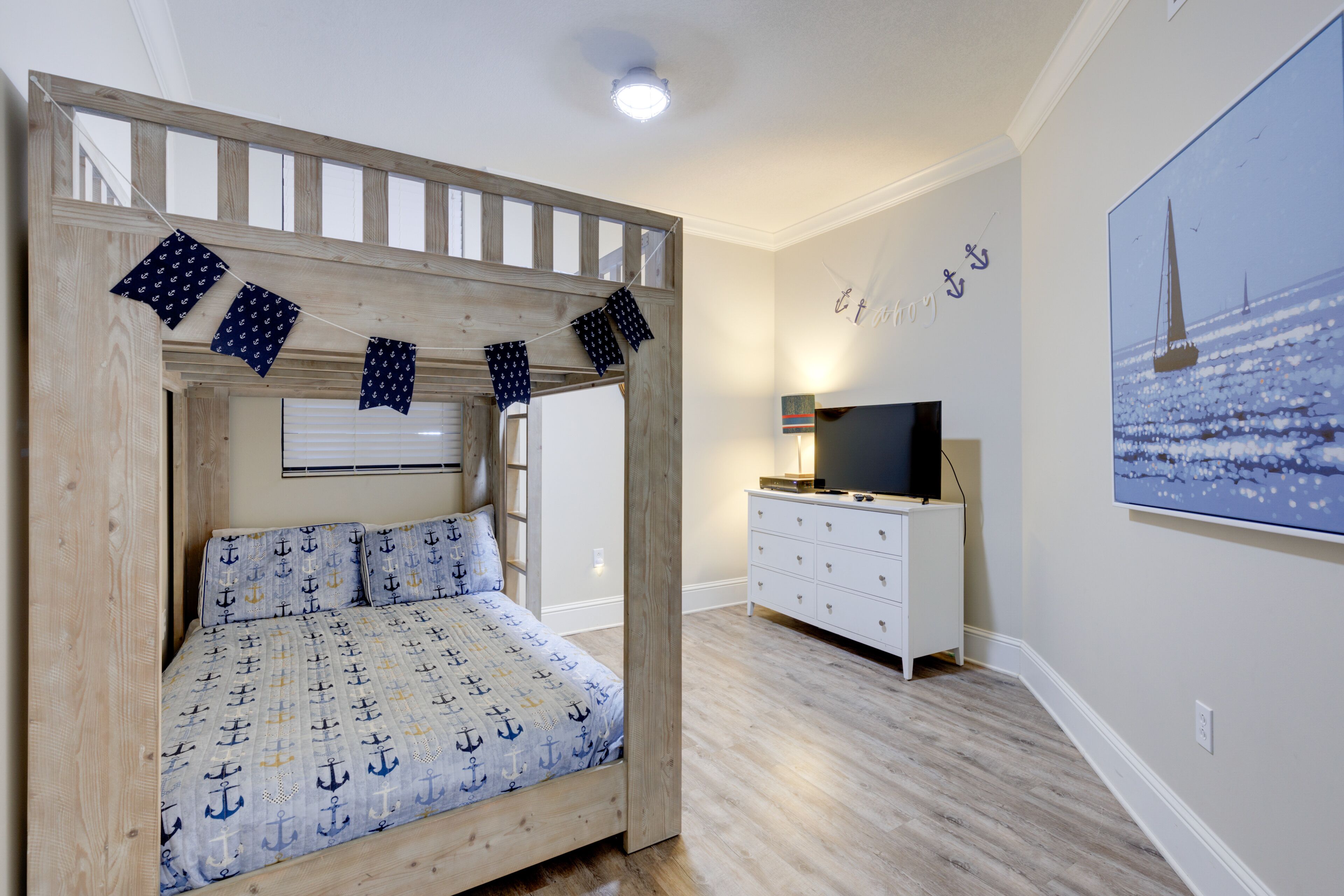 A bedroom with a wooden bed frame, a TV, a dresser, and a painting of a sailboat.