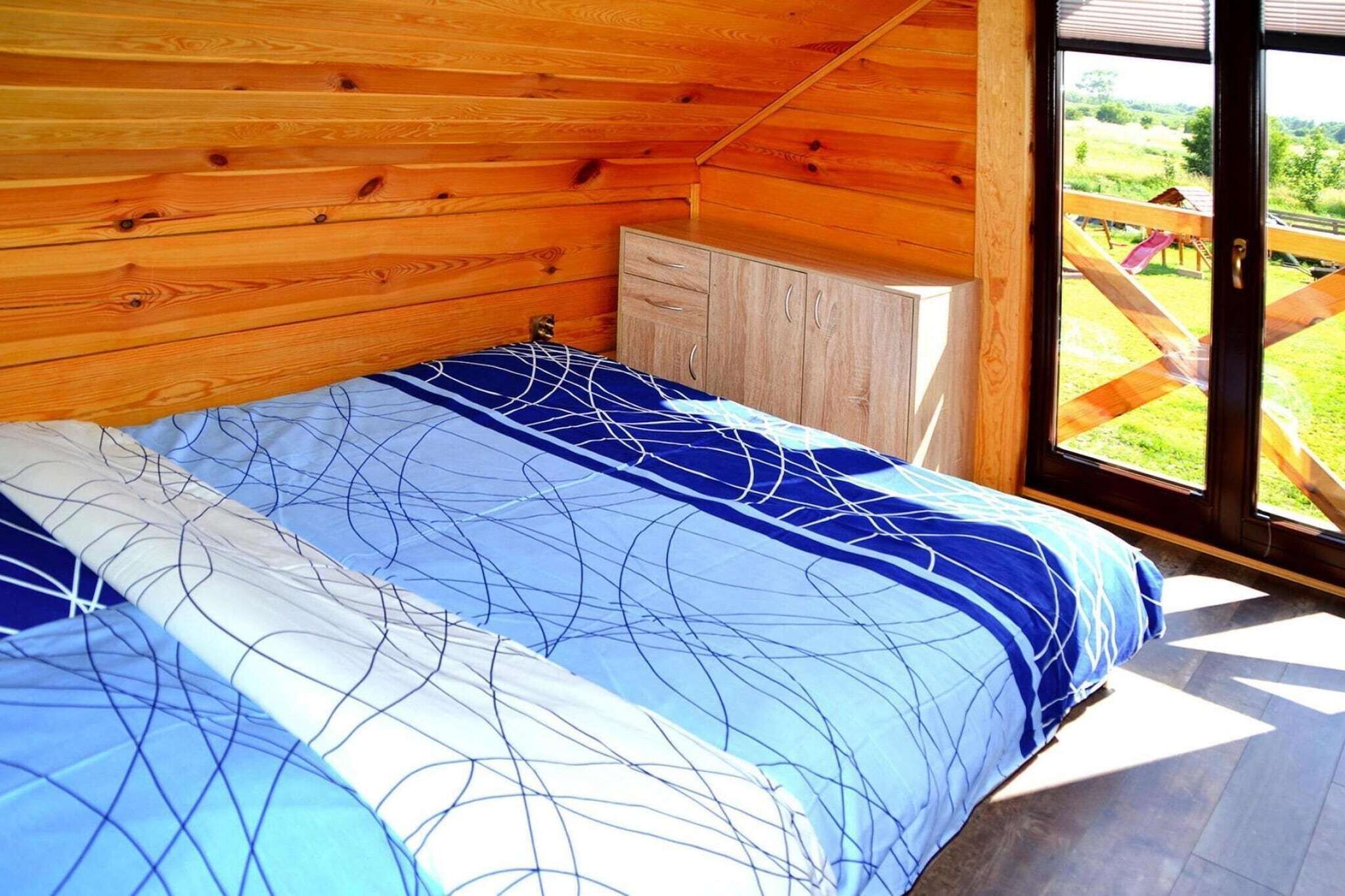 Ein Schlafzimmer mit Bett, Holzwänden, einem Fenster und Blick ins Freie.