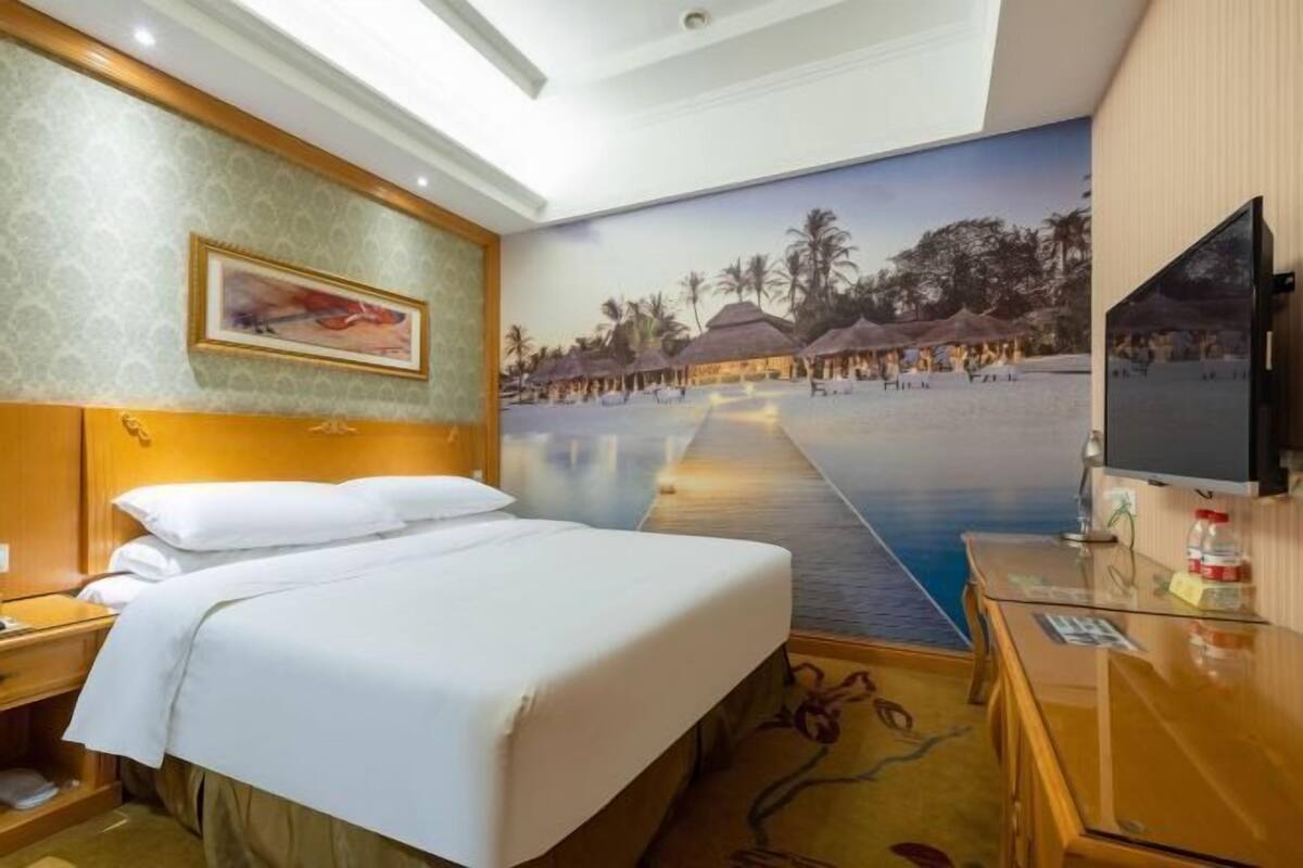 A hotel room with a bed, a desk, a television, and a mural of a beach scene.