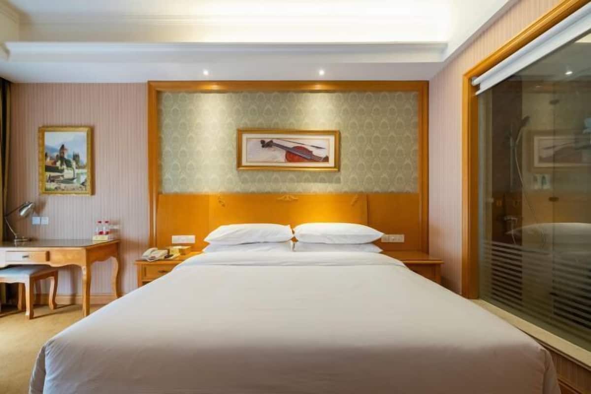 A hotel room with a large bed, a desk, a chair, a nightstand, and a framed picture on the wall.