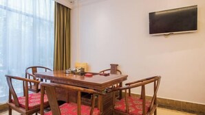 A dining area with a wooden table and chairs, a flat-screen TV on the wall, and a window with curtains. - Vienna Hotel (Kunshan Convention and Exhibition Center) (Kunshan)