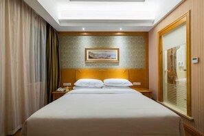 A hotel room with a large bed, a nightstand, a mirror, and a painting on the wall. - Vienna Hotel (Kunshan Convention and Exhibition Center) (Kunshan)