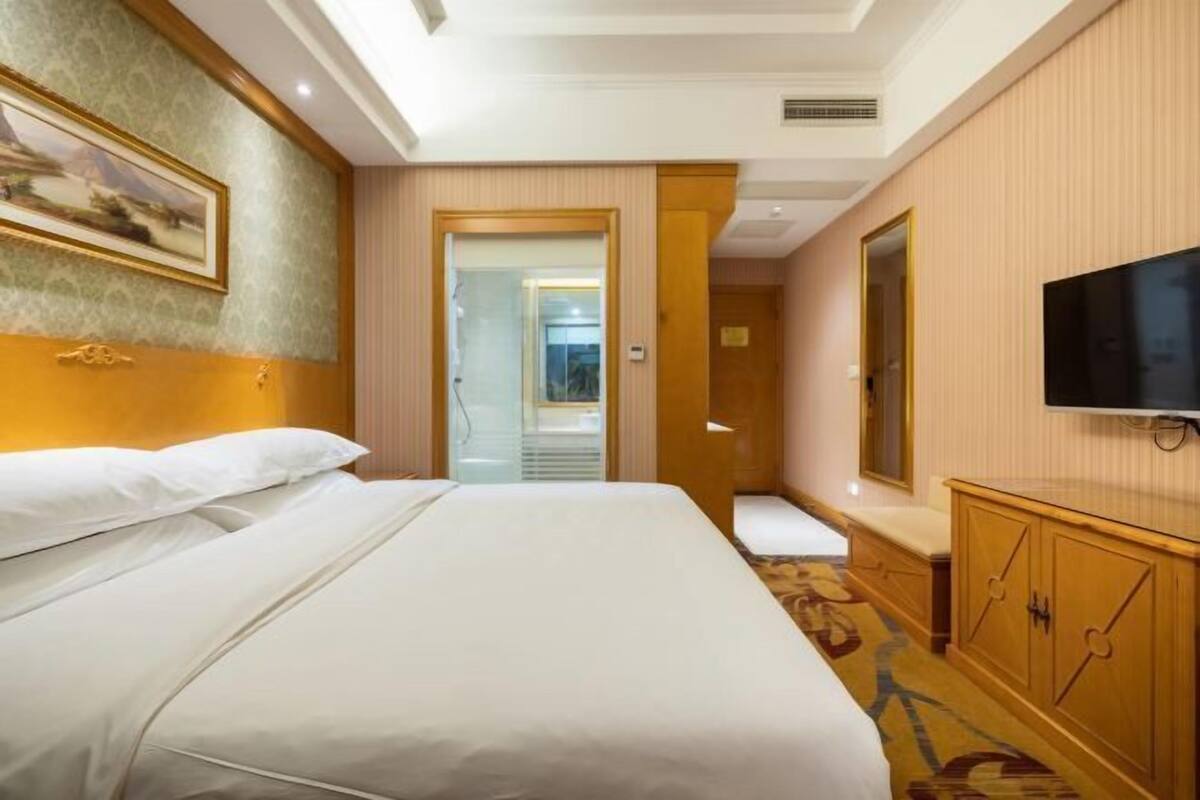 A hotel room with a bed, a television, a wardrobe, and a door leading to another room.