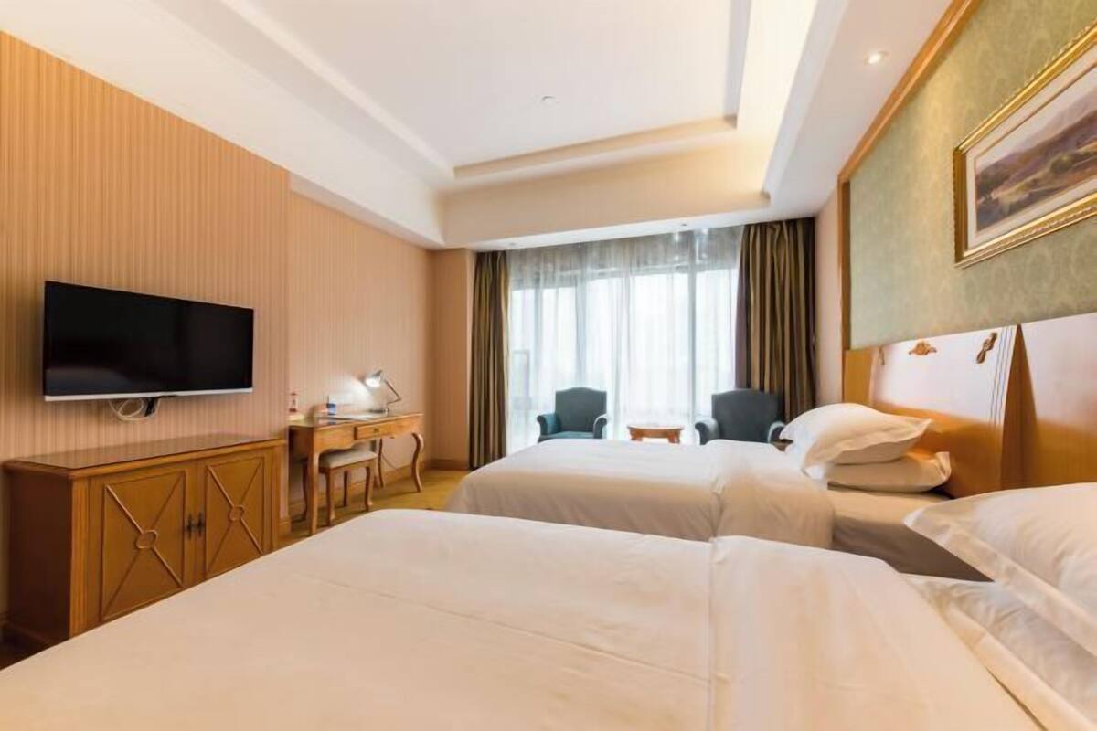A hotel room with two beds, a TV, a desk, and a chair.