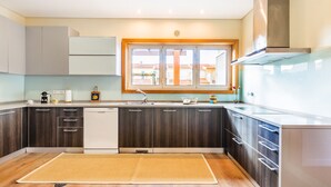 A modern kitchen with dark wood cabinets, a white dishwasher, and a window above the sink. - Furadouro Sunny Family Villa (Ovar)
