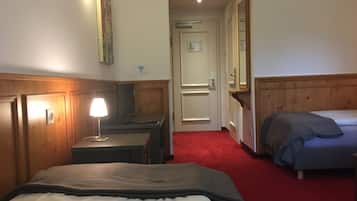 Ein Hotelzimmer mit einem Bett, einem Schreibtisch mit Lampe, einem Computer und einem kleinen Tisch. Eine Tür führt in einen weiteren Raum und an der Wand hängt ein Spiegel.