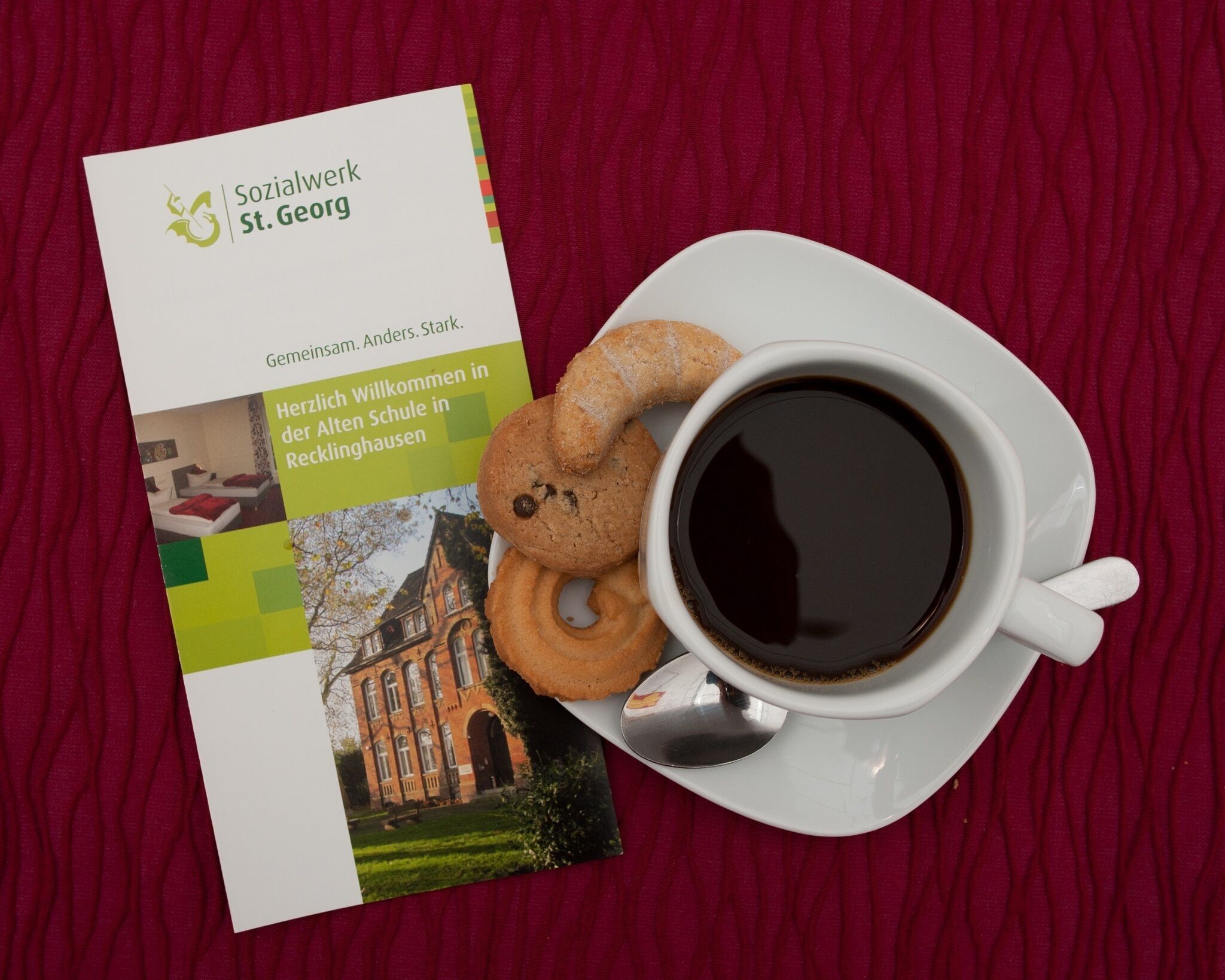 Un folleto titulado 'Sozialwerk St. Georg' con una foto de un edificio, una taza de café y galletas en un plato.