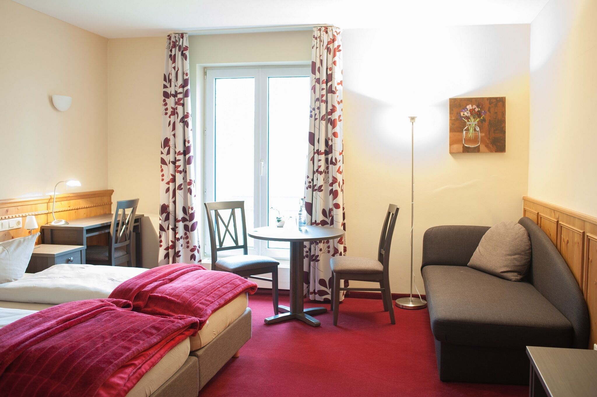 A hotel room with a bed, a desk, a chair, a sofa, and a small table.