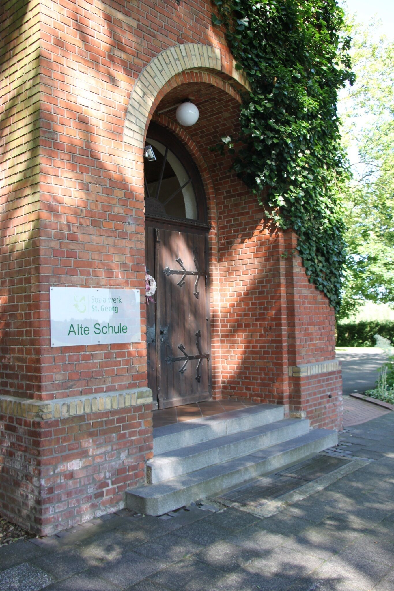 Een gebouw van baksteen met een bord waarop staat: Sozialwerk St.Georg Alte Schule.