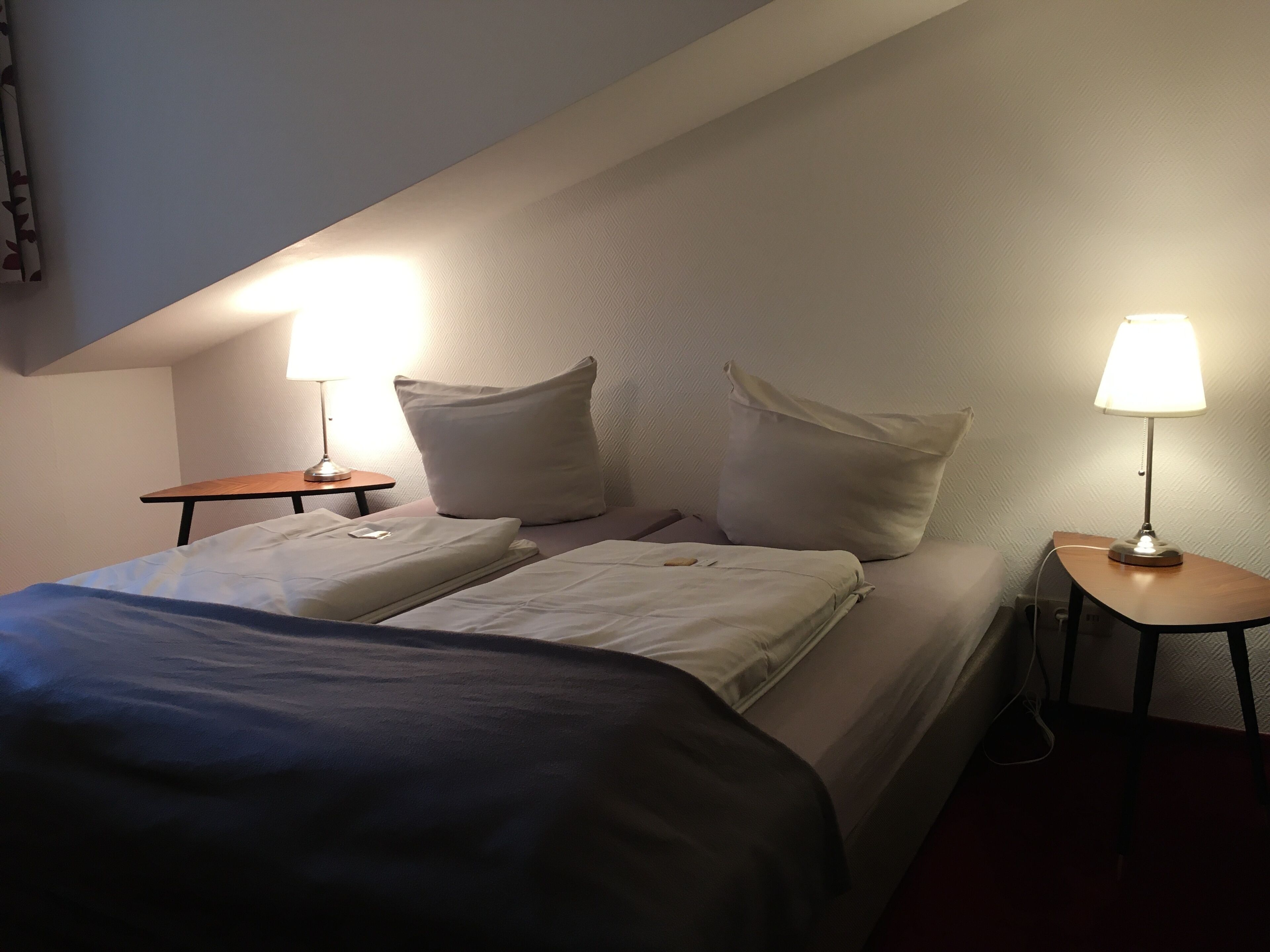 Et hotelværelse med to senge, hver med pude og et natbord med lampe.