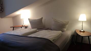 Et hotelværelse med to senge, hver med pude og et natbord med lampe.