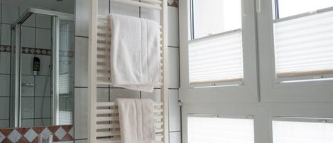 A bathroom with a glass shower enclosure, a towel rack with two towels, and a tiled backsplash.