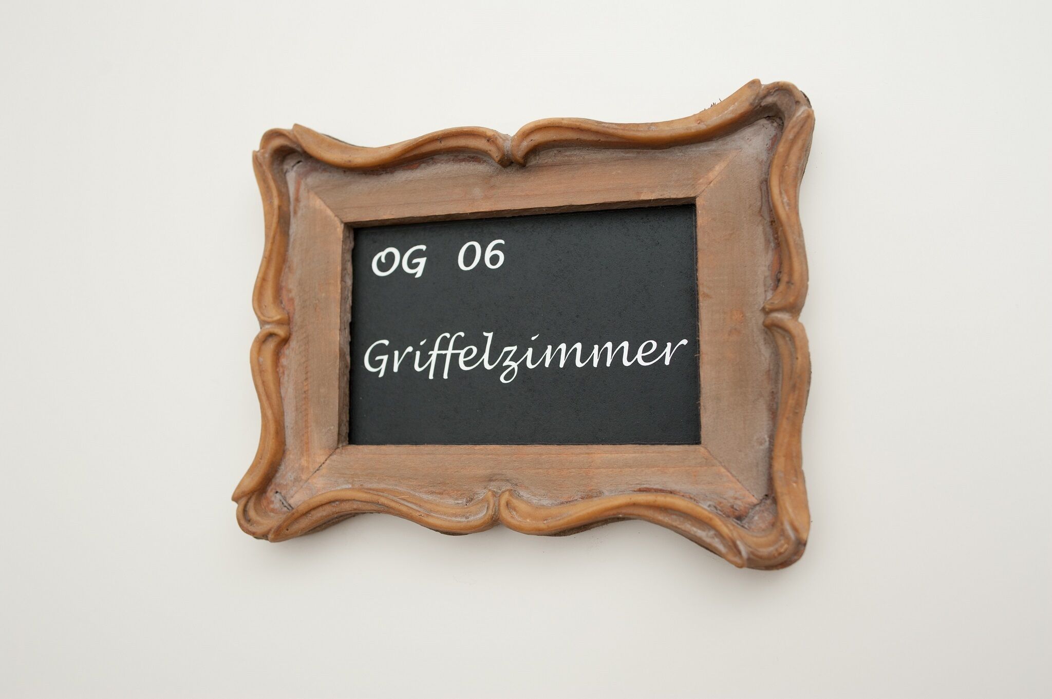 A wooden-framed chalkboard with the text 'OG 06 Griffelzimmer' written on it.