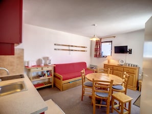 A compact kitchen with a red sofa, wooden dining table, and chairs.