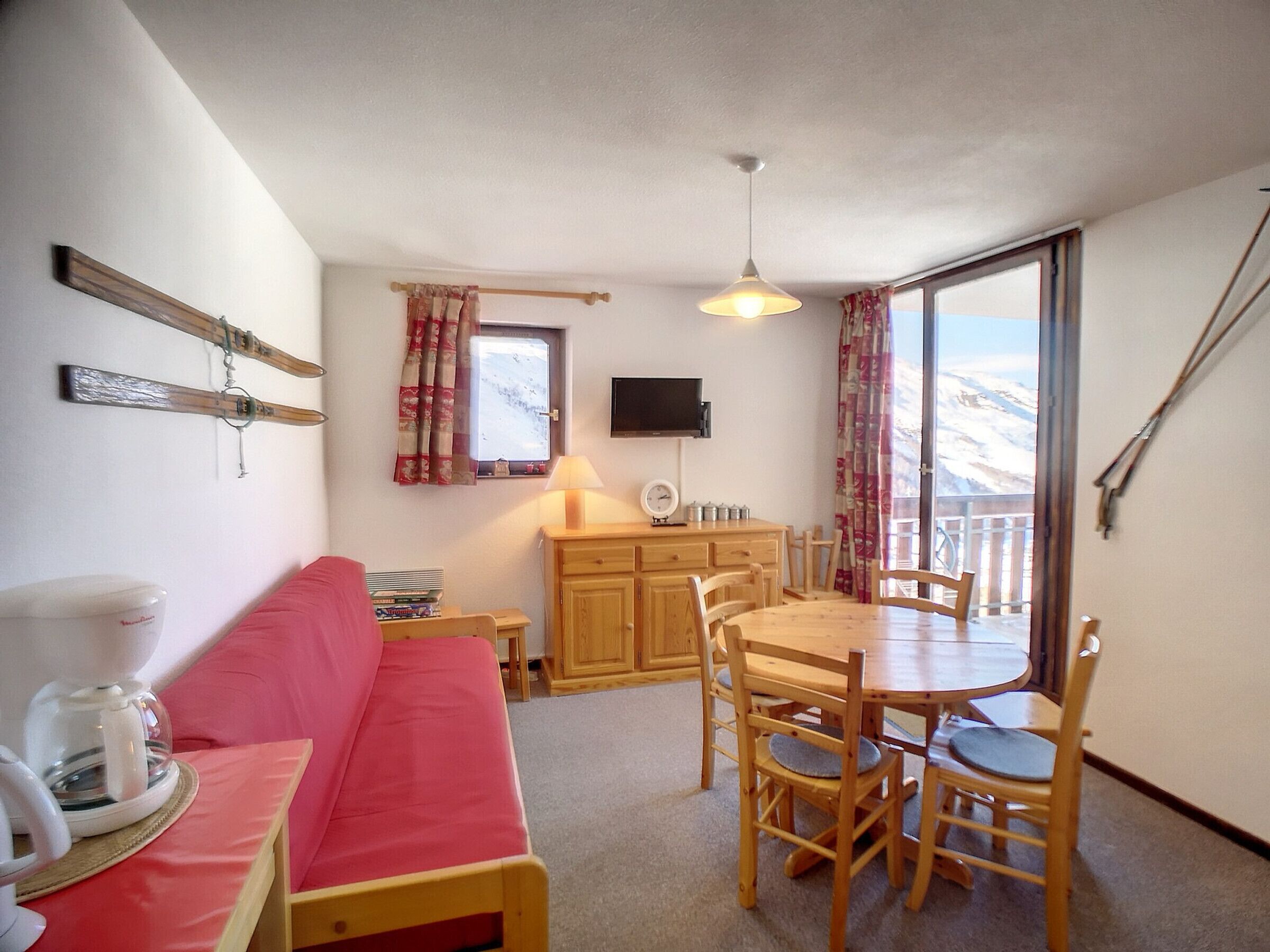 A cozy room with a wooden sofa, a dining table with chairs, a TV, and a window with curtains.