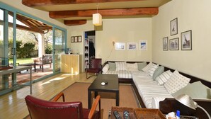 A spacious living room with a wooden ceiling, a large sofa, a coffee table, and a glass door leading to an outdoor area. - Chalet Vignarola (Orbetello)