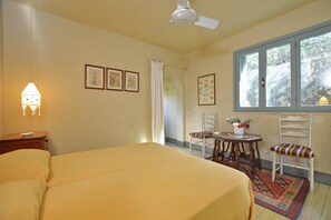 Un dormitorio con cama, ventilador de techo, ventana con vistas, mesa y sillas, y cuadros en la pared.