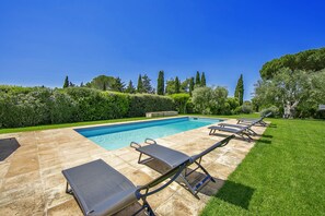 Una piscina con sillones de descanso, un patio de piedra y un césped bien cuidado.