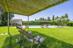 Un espace piscine avec des chaises longues, un patio couvert et un petit abri de jardin.