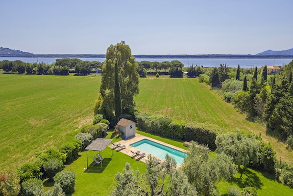 A rectangular swimming pool surrounded by a well-maintained lawn, with a small shed and a gazebo in the foreground. - Chalet Vignarola (Orbetello)