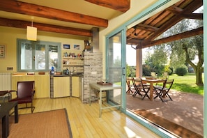 A kitchen with a brick wall, wooden ceiling beams, and a dining area with a table and chairs. - Chalet Vignarola (Orbetello)