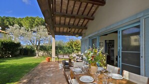 An outdoor dining area with a wooden table set for four, a potted plant, and a view of the garden. - Chalet Vignarola (Orbetello)