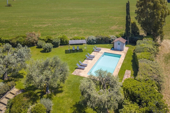 Eine Vogelperspektive eines Anwesens mit Schwimmbad, Liegestühlen, einer kleinen Gartenhütte und umliegender Bepflanzung.