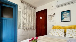 Een slaapkamer met een bed, een blauwe deur, een houten deur, een raam met gordijnen, een airconditioner en een ingelijst schilderij aan de muur.