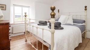 A bedroom with a white bed, a wooden dresser, a window, and a ceiling fan. - Trelash Cottage (Launceston)