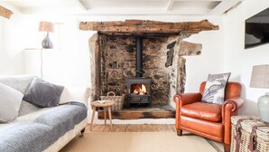 A cozy living room with a stone fireplace, a leather armchair, a sofa, and a small table. - Trelash Cottage (Launceston)