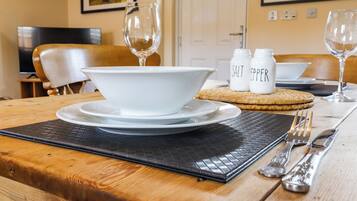A dining table set with white plates, bowls, cutlery, salt and pepper shakers, and a woven placemat.