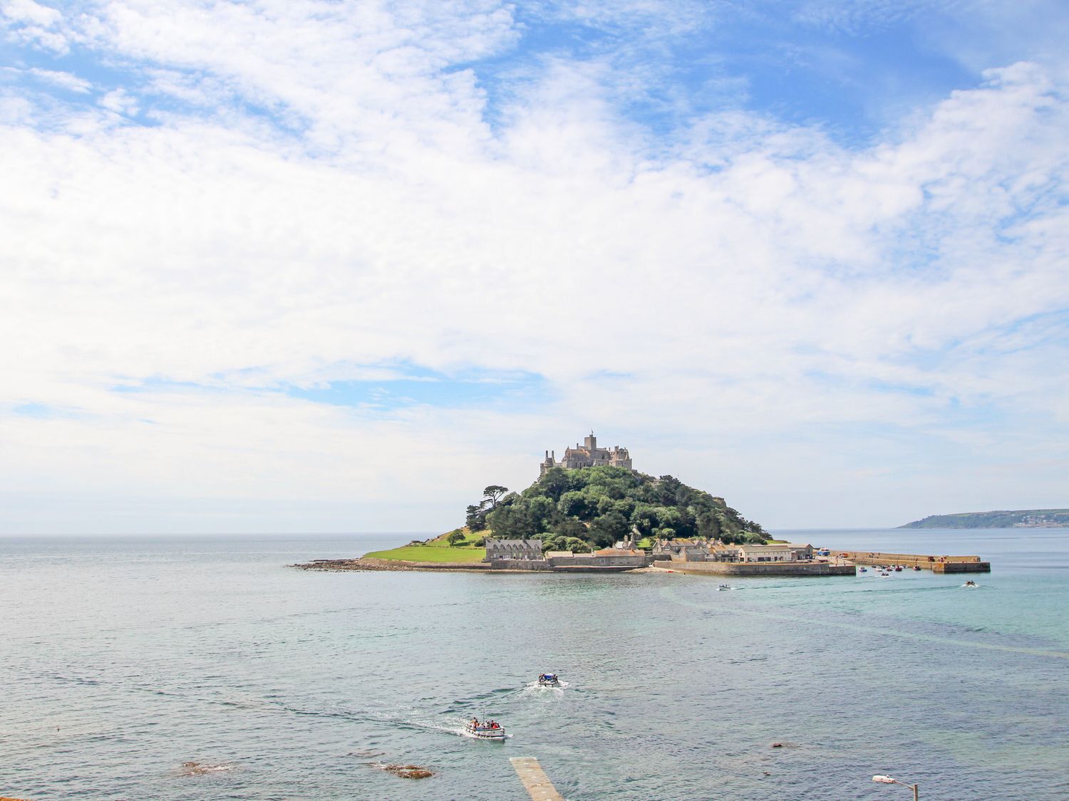 Küstenlandschaft mit einem Schloss auf einer kleinen Insel, blauem Himmel und ruhiger See.