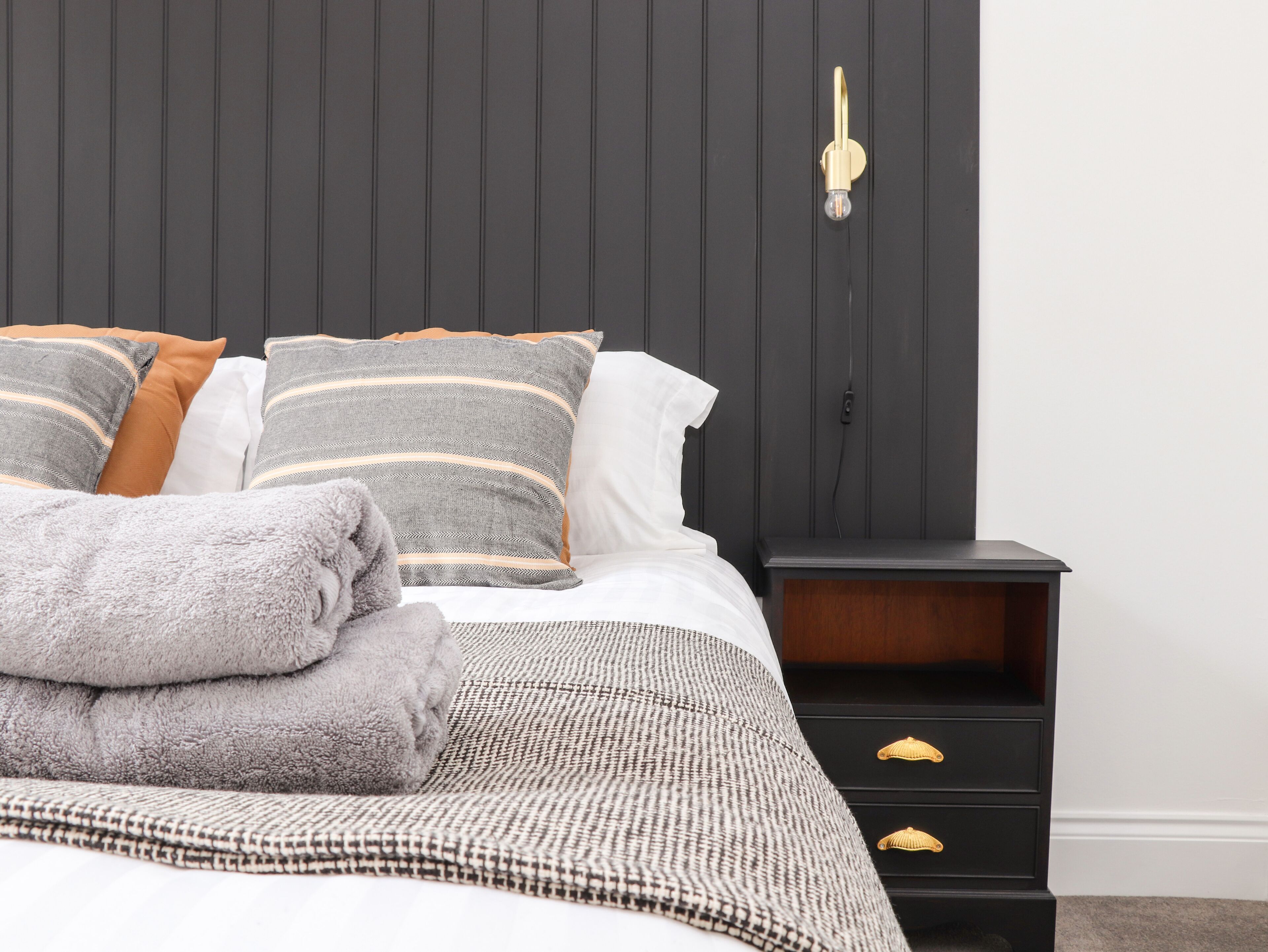 A neatly made bed with striped pillows, a grey fluffy blanket, and a grey towel.