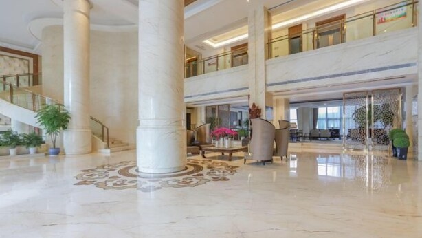 Un amplio vestíbulo con suelos de mármol, grandes columnas, una escalera y una zona de estar con un jarrón de flores.