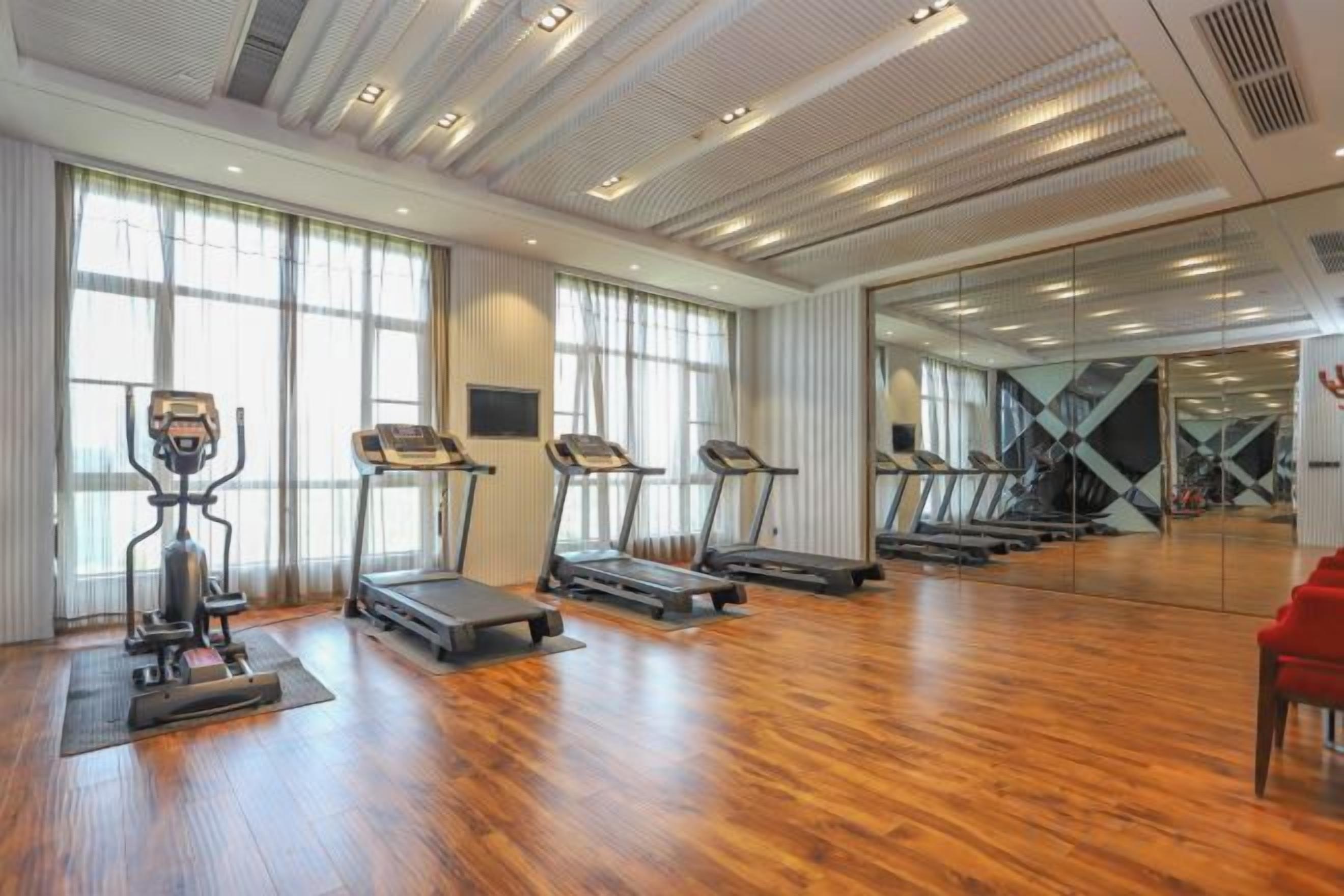 Un gimnasio con cintas de correr, elípticas y un espejo grande.
