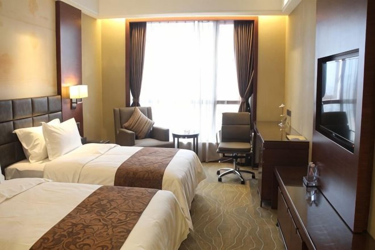 A hotel room with two beds, a desk, a chair, a TV, and a window with curtains.
