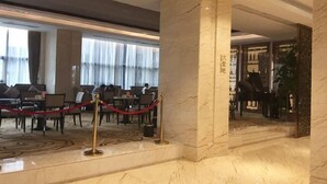 Un hall de hotel con piso de mármol, una recepción y una zona de estar con mesas y sillas.