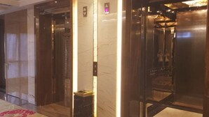 Vestíbulo de hotel con suelo de mármol, mostrador de recepción y dos ascensores.