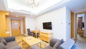 A hotel room with a sofa, a small table, a TV, and a door leading to another room. - Vienna Hotel (Jiangmen Wanda Plaza Store) (Jiangmen)