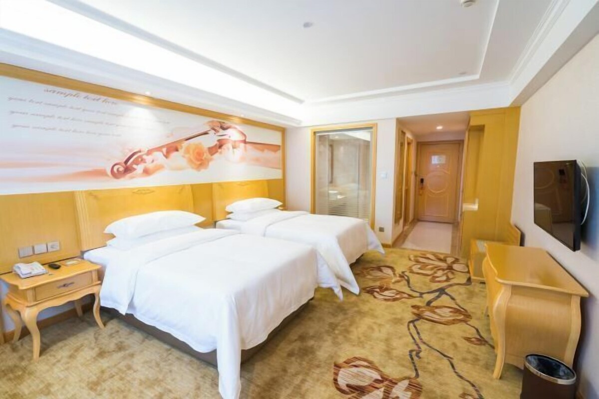 A hotel room with two beds, a desk, a TV, and a large poster on the wall.