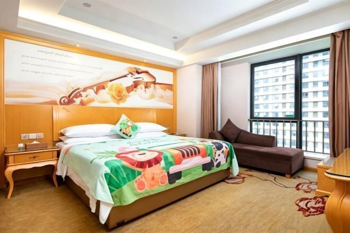 A hotel room with a bed, a sofa, a large window, and a wall with a poster.