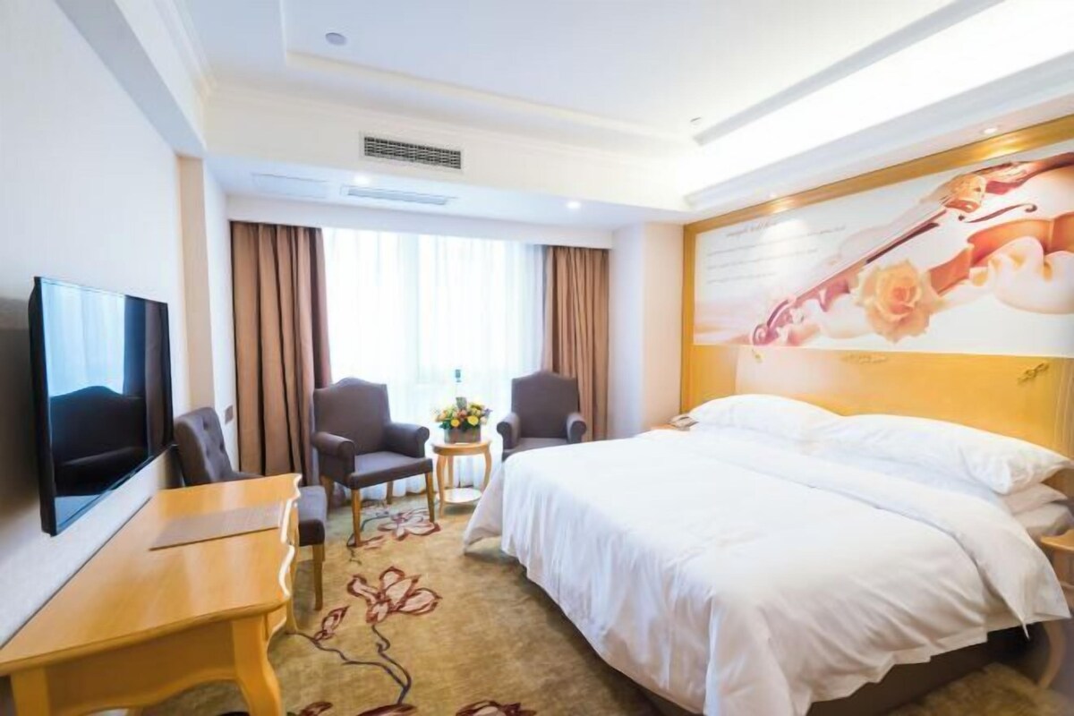 A hotel room with a bed, a desk, a chair, a TV, and a window with curtains.