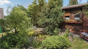 Une cabane en bois avec un étang, entourée d’une végétation luxuriante et d’arbres.