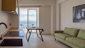 A modern living room with a green sofa, a dining table with chairs, a kitchen area with a stove, and a balcony with a view. - Apartment Biancolilla - Maina Country Resort - with pool, in Sicily (Naso)