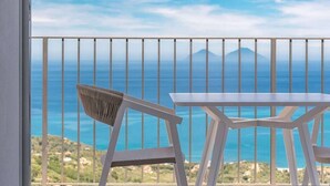 A balcony with a white table and chair, overlooking a coastal view with a mountain in the distance. - Apartment Biancolilla - Maina Country Resort - with pool, in Sicily (Naso)