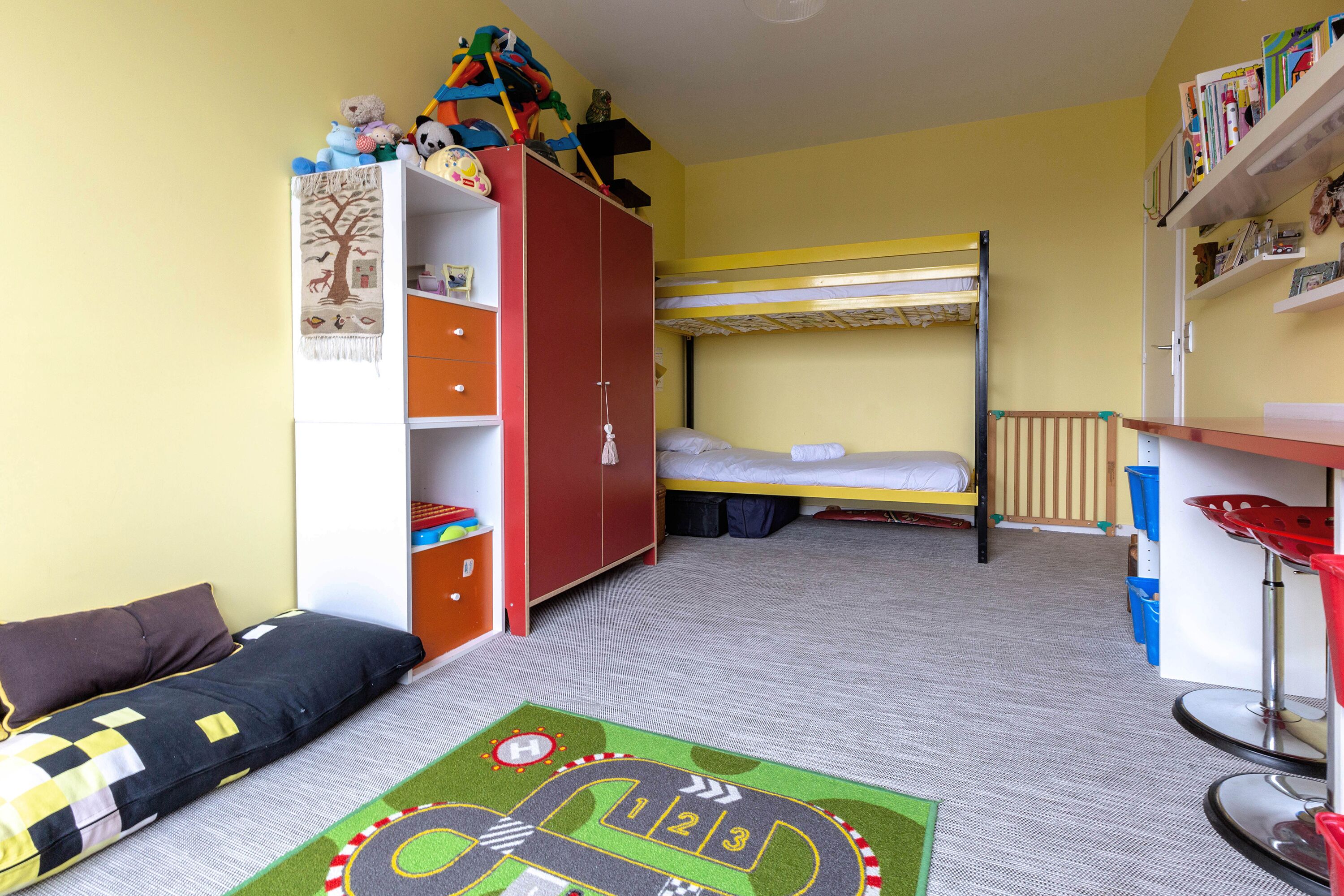 Quarto de criança com beliches, guarda-roupa, escrivaninha e tapete de brincadeira.