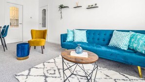A modern living room with a blue sofa, yellow armchair, and a coffee table. There are three shelves with plants on the wall. - One Bedroom Apartment by Klass Living Serviced Accommodation Hamilton - Back'O'Barns Apartment With WiFi (Hamilton)