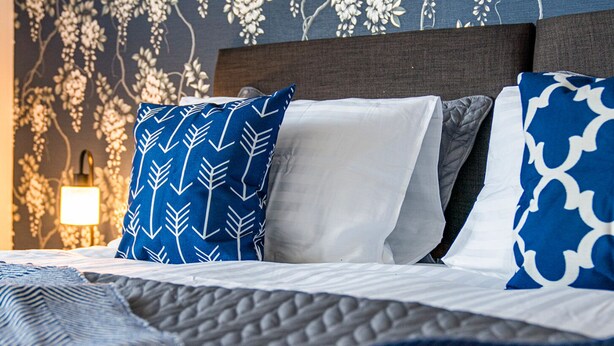 A neatly made bed with a patterned blue pillow, a plain white pillow, and a patterned blue pillow on a dark headboard. - One Bedroom Apartment by Klass Living Serviced Accommodation Hamilton - Back'O'Barns Apartment With WiFi (Hamilton)