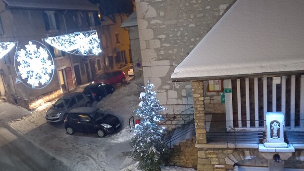 Una strada innevata con un edificio in pietra, un piccolo albero di Natale e una fontana.