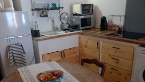 Una cucina compatta con un tavolo da pranzo, sedie, una ciotola di frutta, una lavatrice e un forno a microonde.
